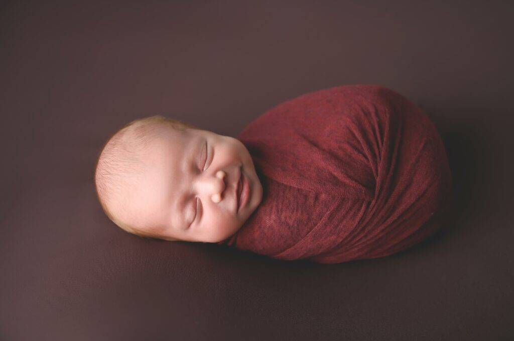 A newborn baby boy wrapped in a red wrap.