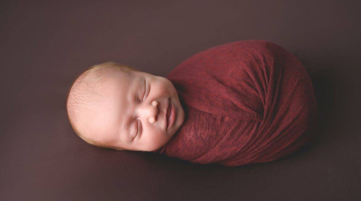 A newborn baby boy wrapped in a red wrap.