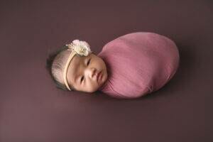 A baby girl wrapped in a pink blanket on a brown background.