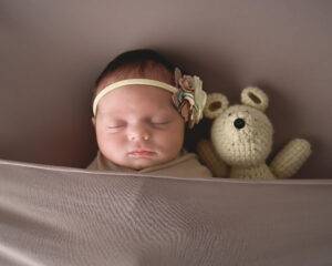 A baby sleeping with a stuffed bear.