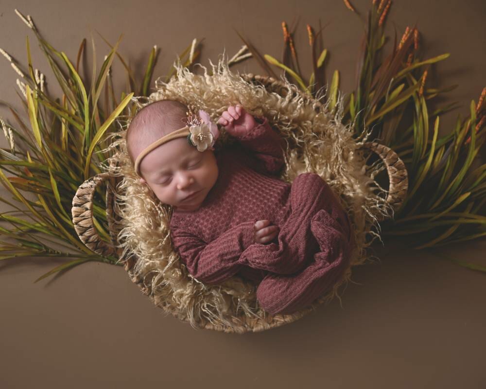 A newborn girl is laying in a basket of grass.