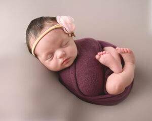 A newborn girl wrapped up in a purple wrap.