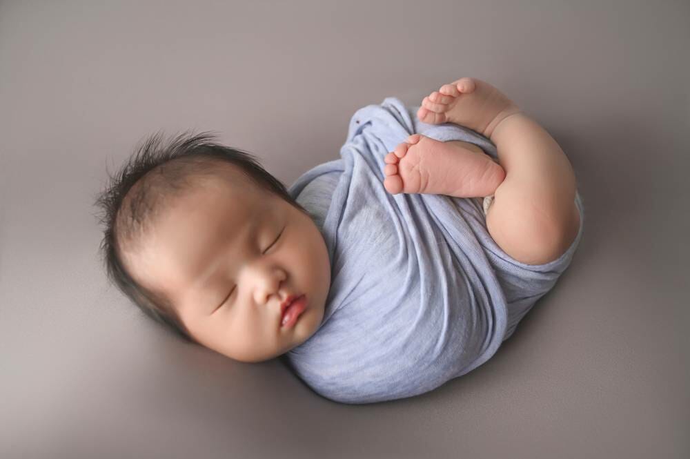 A baby boy wrapped in a blue blanket on a gray background.