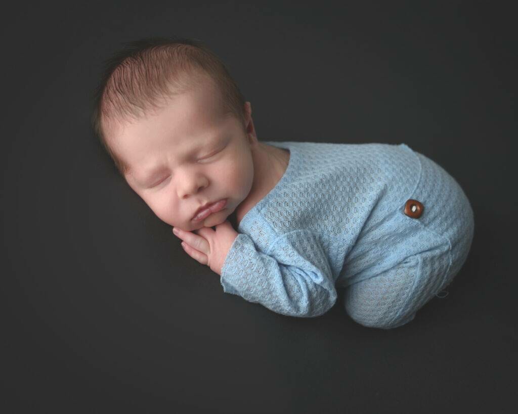 A baby boy is laying down on a black background.
