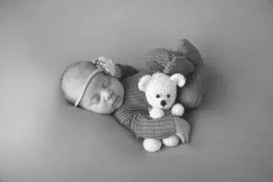 A black and white photo of a baby sleeping with a teddy bear.