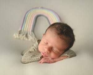A newborn baby sleeping in front of a rainbow.