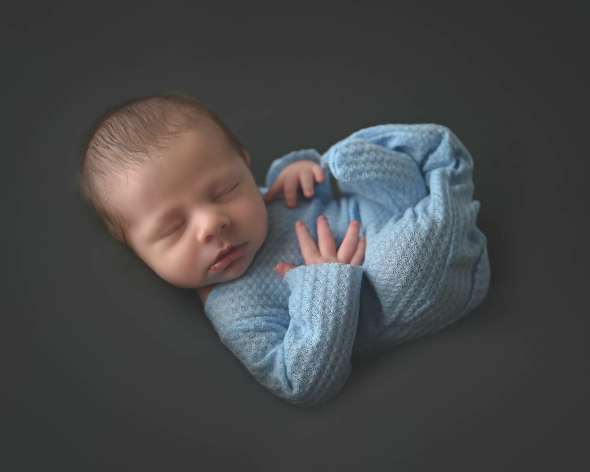 A newborn baby boy is laying on a dark background.