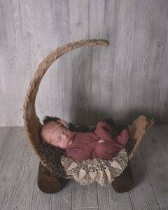 A newborn sleeping in a wooden cradle.