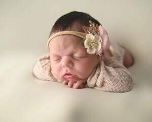 A baby girl is laying on a white background with a flower headband.