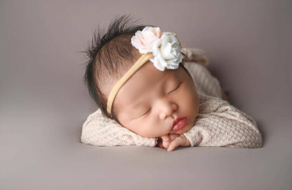 A baby girl laying on a gray background with a flower headband.