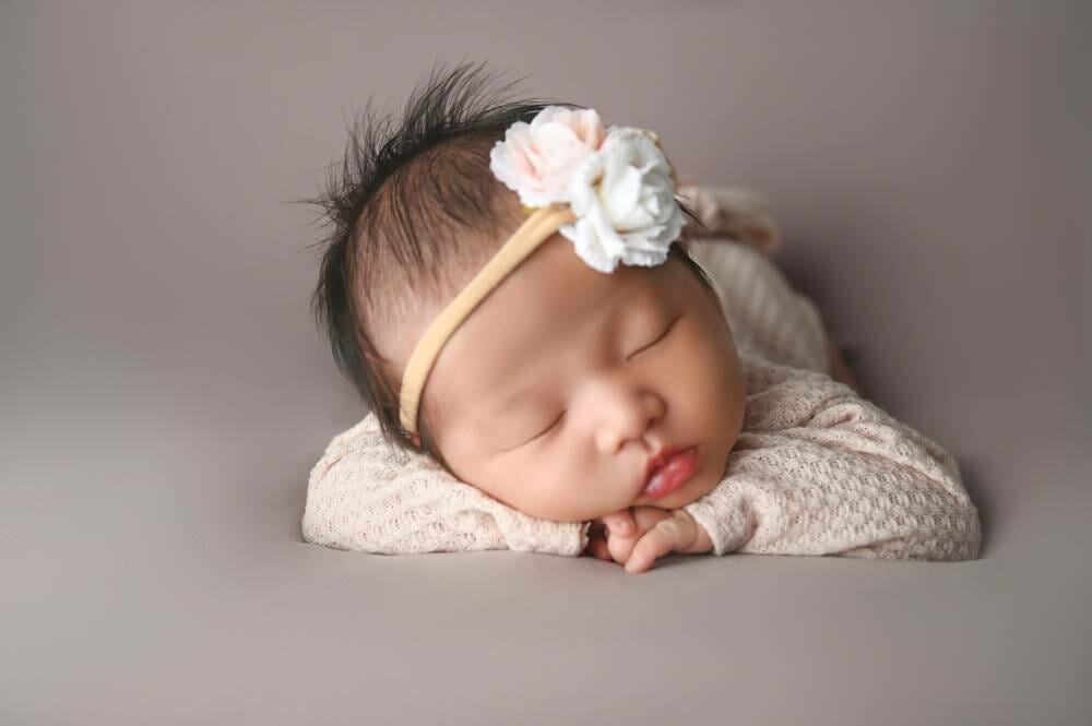 A baby girl laying on a gray background with a flower headband.