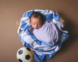 A baby is wrapped in a blanket with a soccer ball.