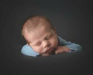 A baby boy is sleeping on a dark background.