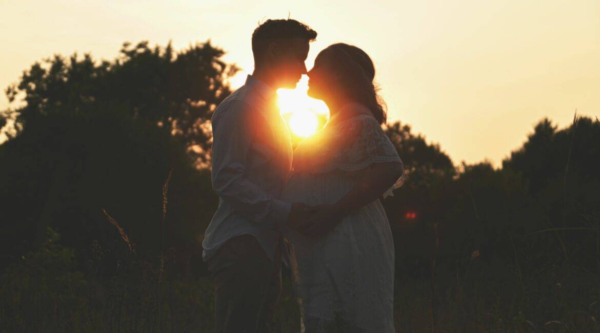 A couple kisses at sunset in a field.