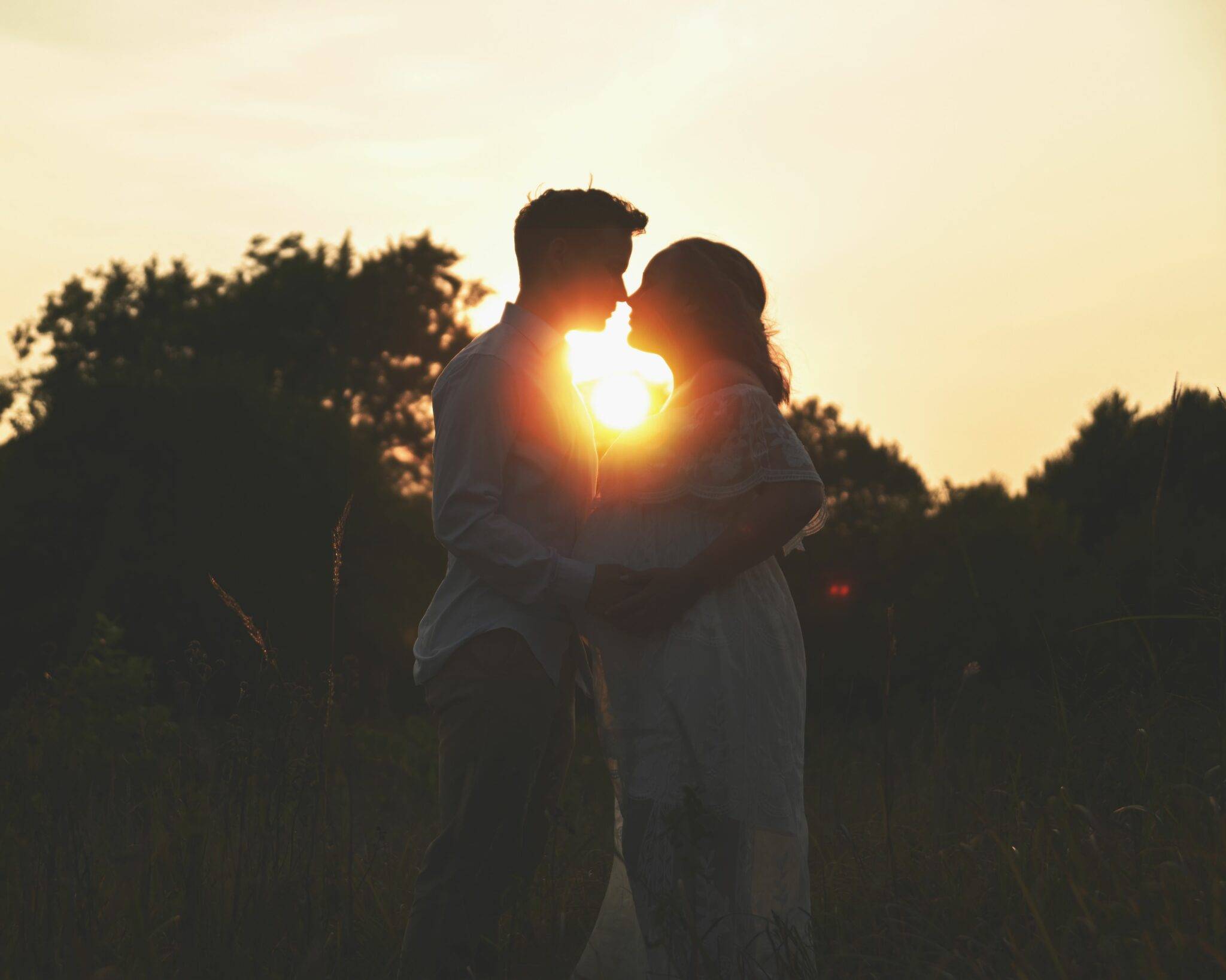 A couple kisses at sunset in a field.