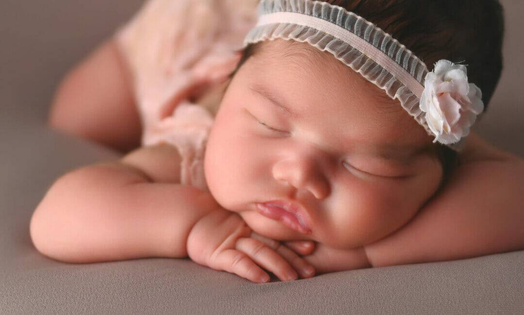 newborn baby girl with head on hands, posing in studio