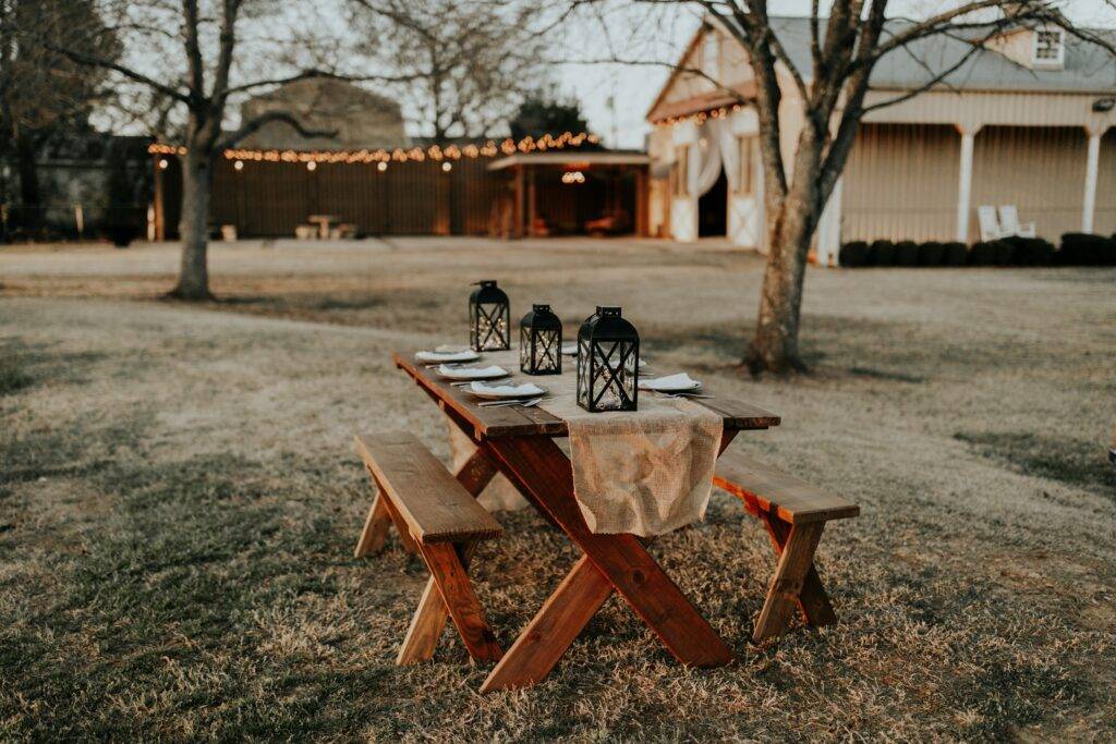 A picnic table set up in a field with lanterns.