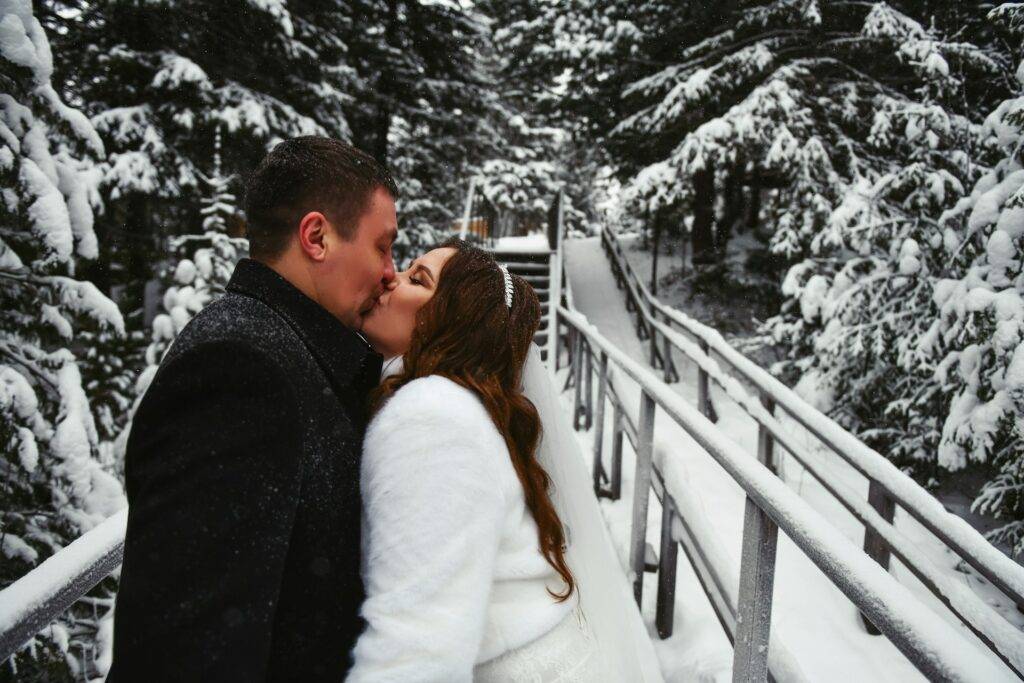 A bride and groom kissing on a bridge in the snow.