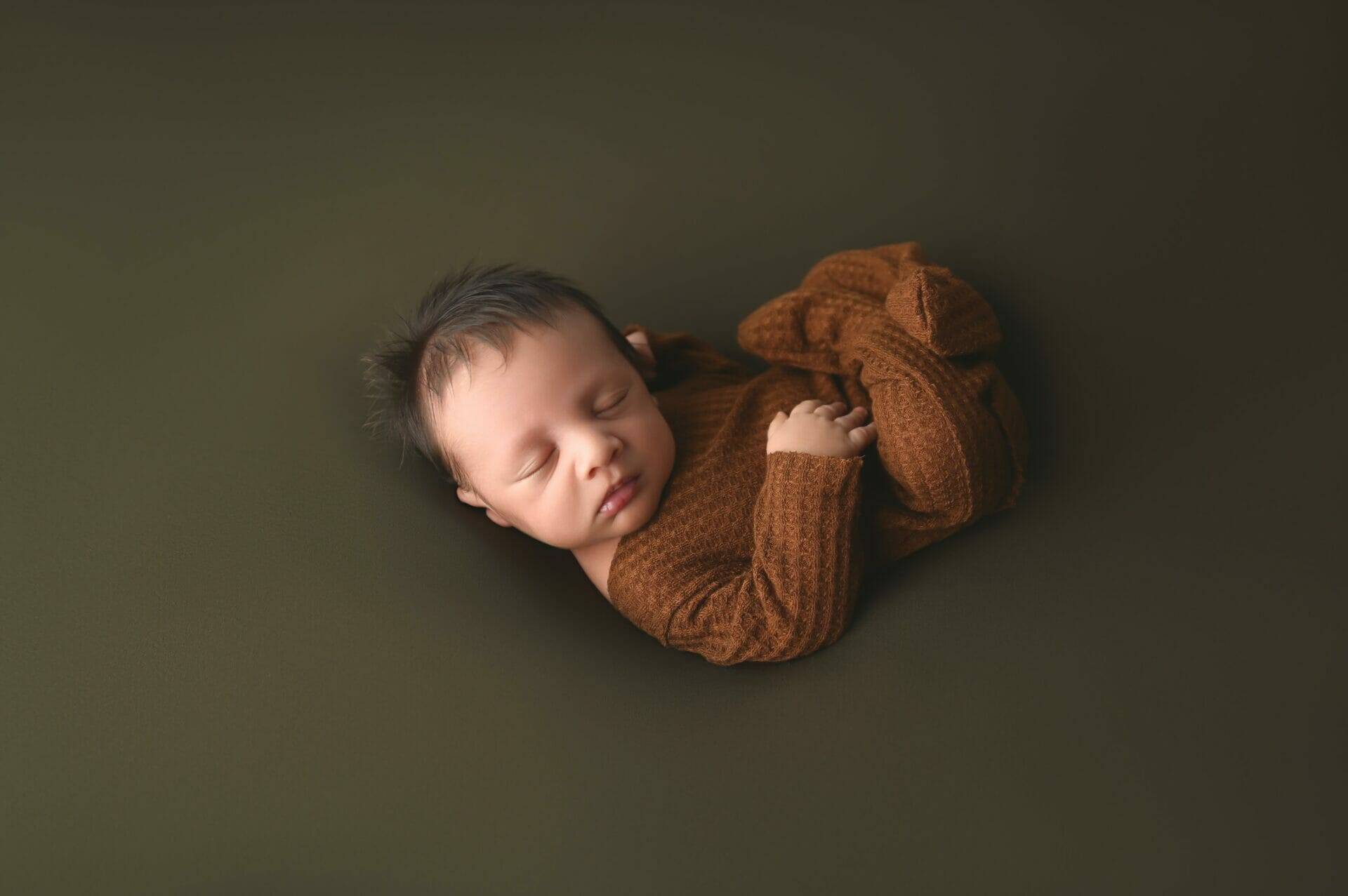 posed newborn baby on green background with brown outfit on