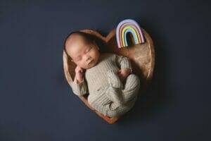 newborn baby boy in a heart bowl with a rainbow prop near him