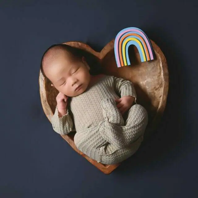 newborn baby boy in a heart bowl with a rainbow prop near him