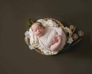 A newborn baby in a basket on a brown background for newborn photography.