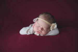 A newborn girl peacefully resting on a maroon background in Saint Paul, Minnesota.