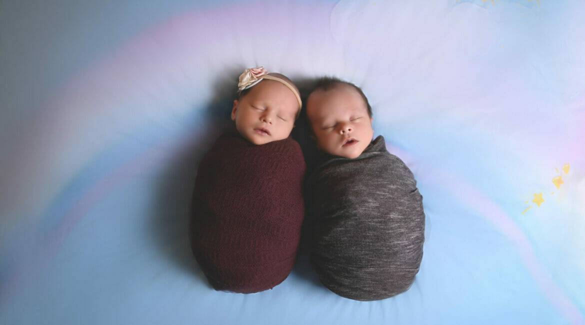 twin newborns wrapped laying on a rainbow background, newborn photography