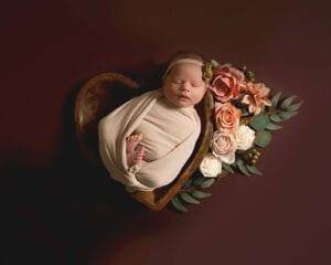 A newborn girl is peacefully resting in a heart-shaped box surrounded by flowers in this stunning newborn photography shot. Located in Minnesota, this maternity photographer perfectly captures the beauty of new life.