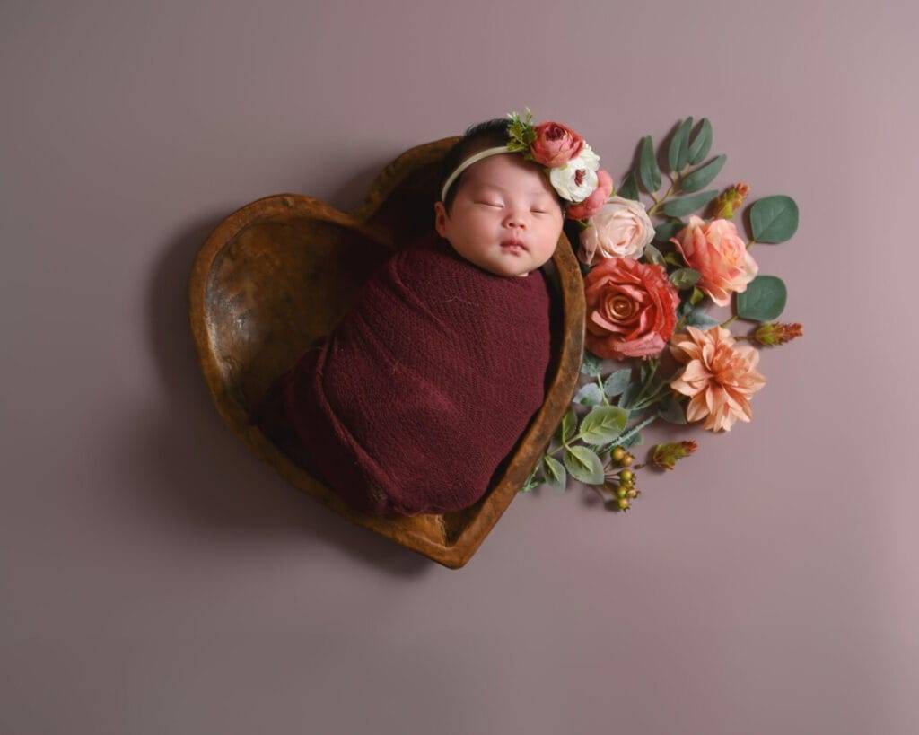 Capture the precious moment of a newborn girl in a heart-shaped wooden bowl with stunning newborn photography.