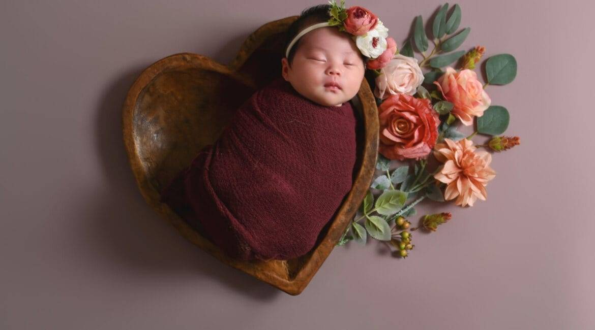 Capture the precious moment of a newborn girl in a heart-shaped wooden bowl with stunning newborn photography.