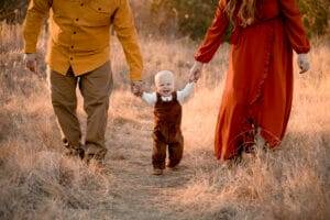 A family holding hands while walking through a field at sunset.