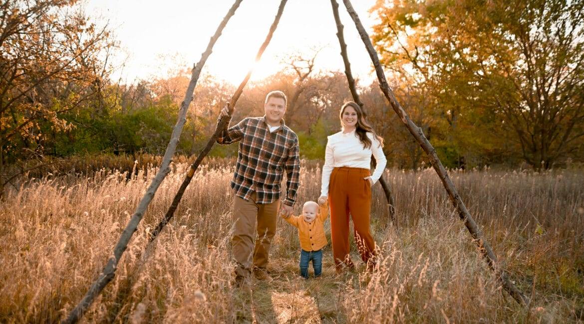 A family is standing in a field with a teepee in the background.