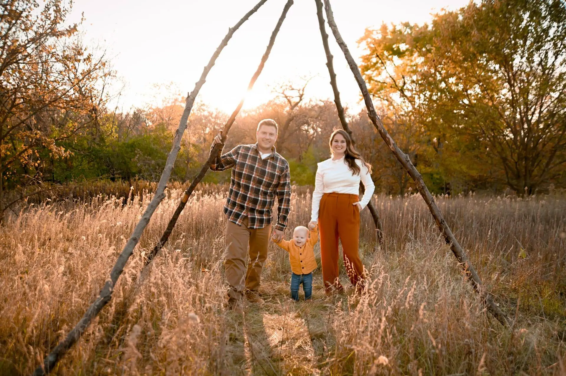 A family is standing in a field with a teepee in the background.