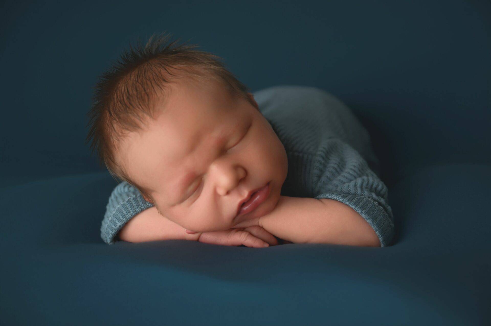 Newborn baby sleeping peacefully in a blue outfit, resting on a soft surface.