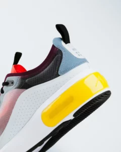 Close-up of a modern sneaker with a mixed-material upper, featuring a yellow and white sole with visible air cushioning and a black and white outsole.
