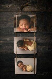 Three photos of a sleeping baby in different poses are hung vertically on a dark wooden surface with twine.