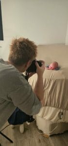 Person with short hair taking a photo of a baby lying on a beige blanket covering a table.