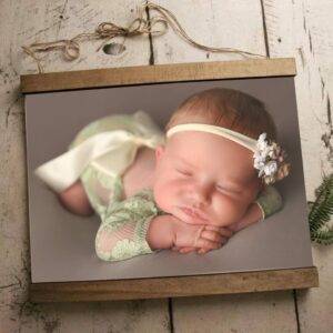 A baby in a green lace outfit and headband sleeps on a wooden frame background.