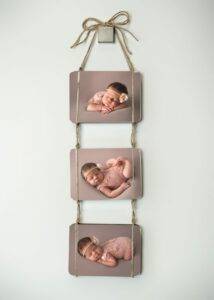 Wall decoration featuring three photos of a sleeping baby in pink outfits, displayed on a vertical string with a bow at the top.