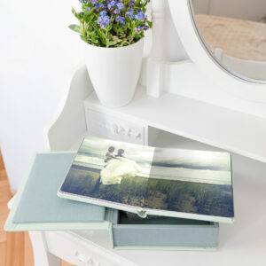 Open photo album with a wedding picture of a couple on a grassy field. The album is on a light blue box, placed on a white dresser with a potted plant and a mirror.