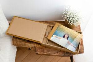 A photo album on a wooden table beside a vase of small white flowers. The album is open, showing an image of a woman in a white dress, relaxing with her eyes closed.