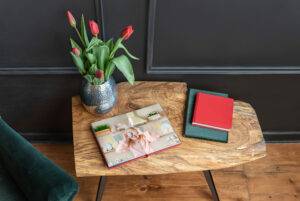 Wooden table with a vase of red tulips, an open photo album showing a child, and two closed books on a wooden floor.