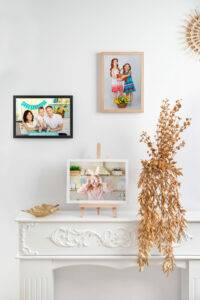 Wall and mantel display photos of families and children, with a bundle of dried leaves on a decorative white mantel.
