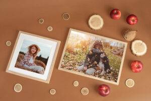 Two framed photos on a brown surface, surrounded by coins, wooden slices, apples, and a walnut. One photo shows a child outdoors; the other depicts a child with a dog in autumn leaves.