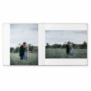 An open photo album shows two images of a couple embracing in a grassy field under a cloudy sky.