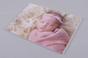 A sleeping baby wrapped in a pink blanket and wearing a pink headband, lying on a fluffy cream surface.