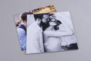 Two photo books on a gray surface. The top book has a black-and-white image of a couple embracing closely. The bottom book features a blurred color image of a person with flowers in the background.