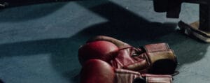 A pair of red boxing gloves resting on a dark floor under a shadow.