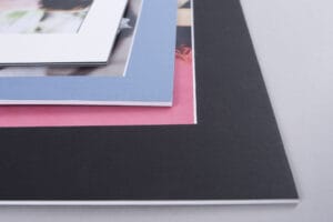 Close-up of four stacked picture frames with different colored mats: white, blue, pink, and black, lying on a light gray surface.
